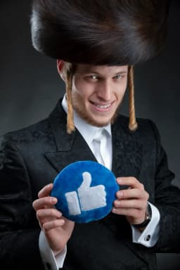 צילום תדמית עם אביזר: גבר בכובע פרווה מסורתי ובחליפה שחורה מחזיק כרית בצורת סמל ״לייק״ — צילום מושגי על רקע כהה